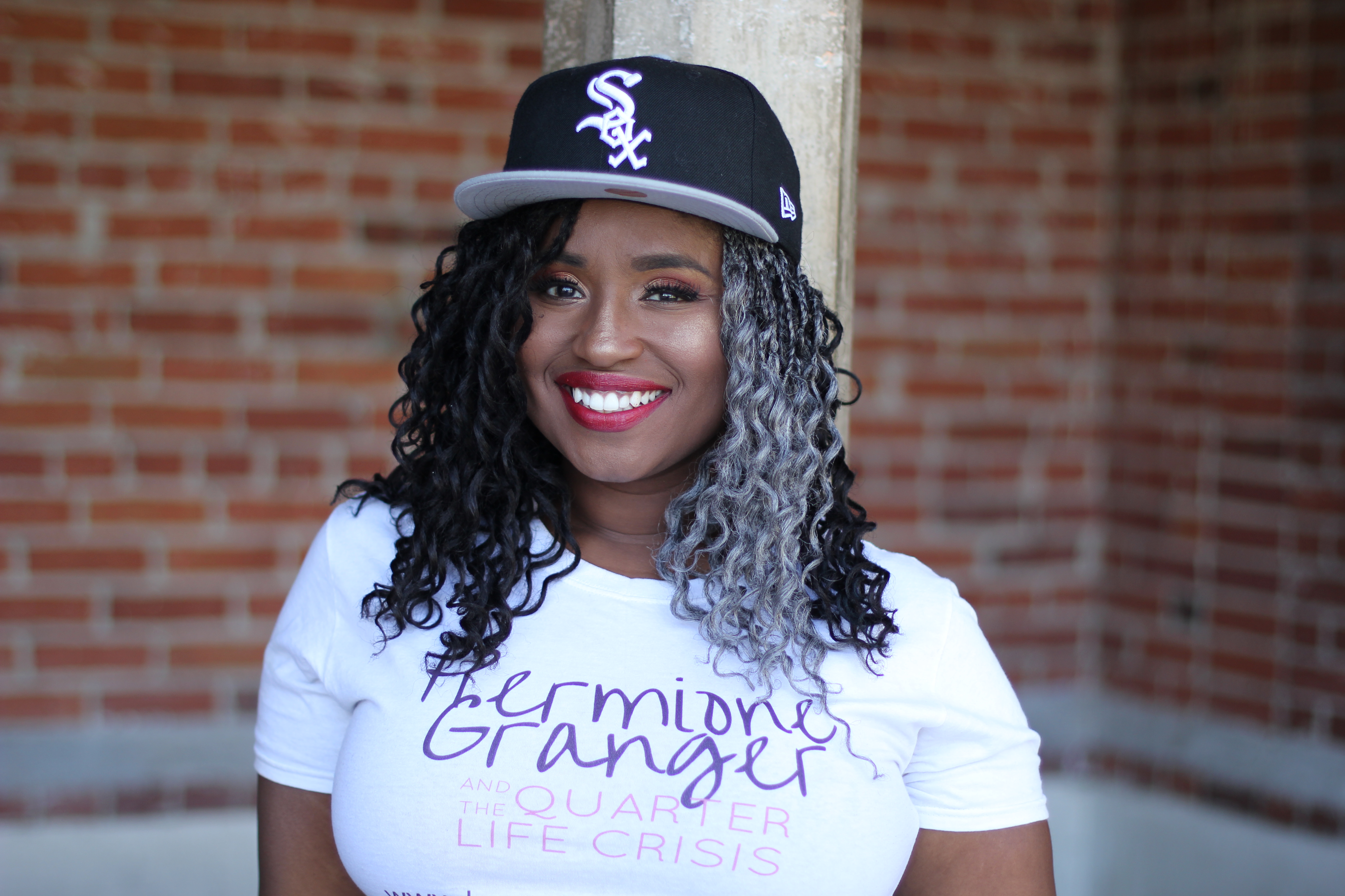 Eliyannah in front of a brick wall wearing a white t-shirt and black Chicago White Sox hat